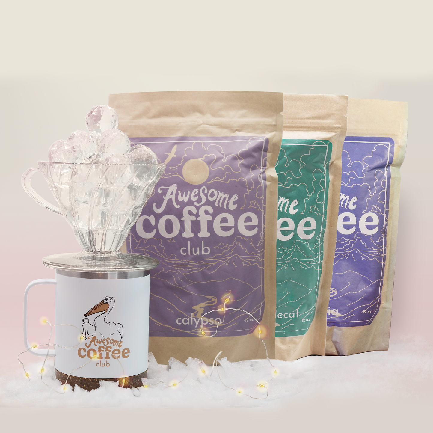 A photo of the three different bags of Awesome Coffee lined up behind the Awesome Coffee Club holiday travel mug and pour over filled with shiny, crystal balls. A Good Store product.