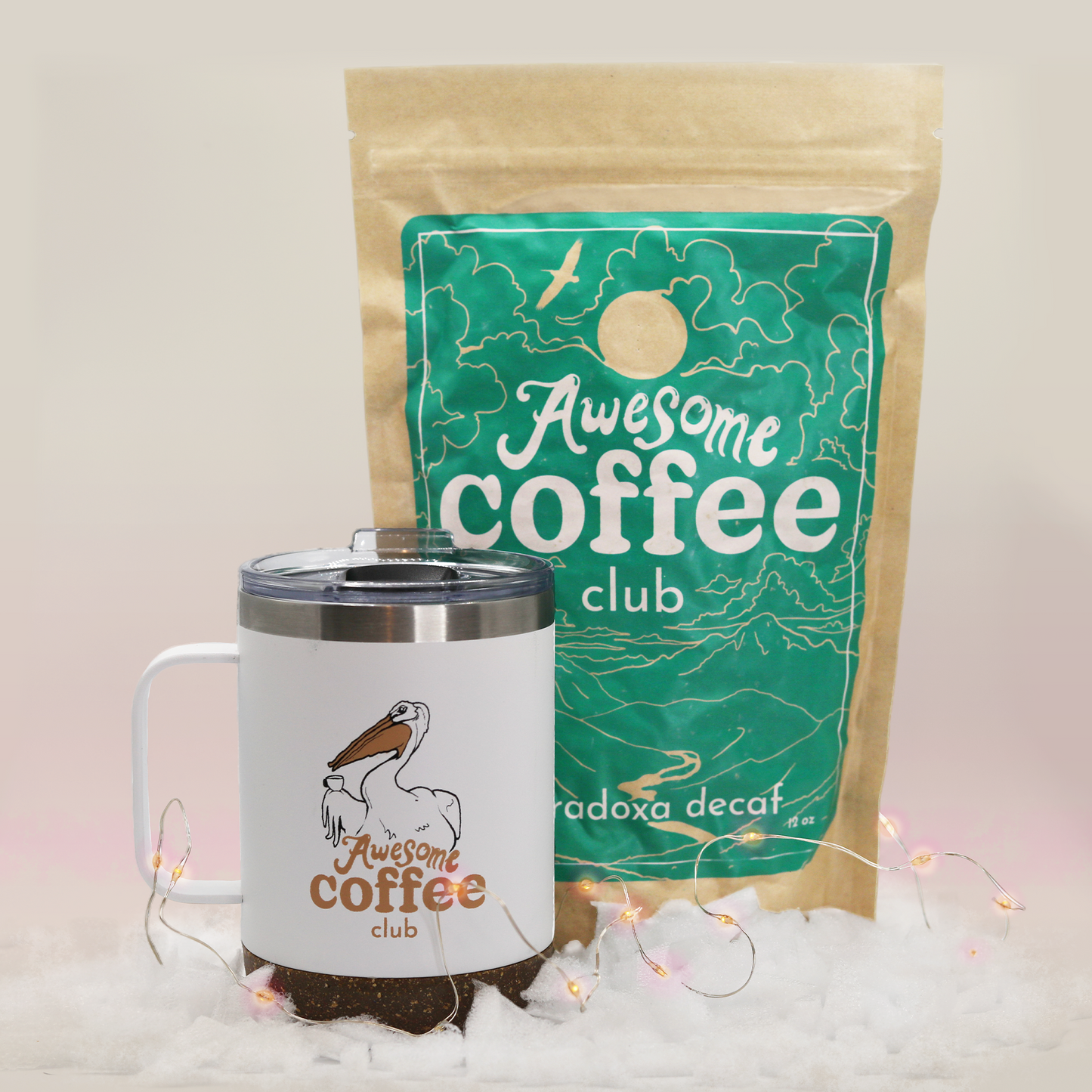 A bag of Paradoxa decaf coffee from the Awesome Coffee Club with a dark green label sits behind a white travel mug with a pelican and the Awesome Coffee Club logo. A Good Store product.