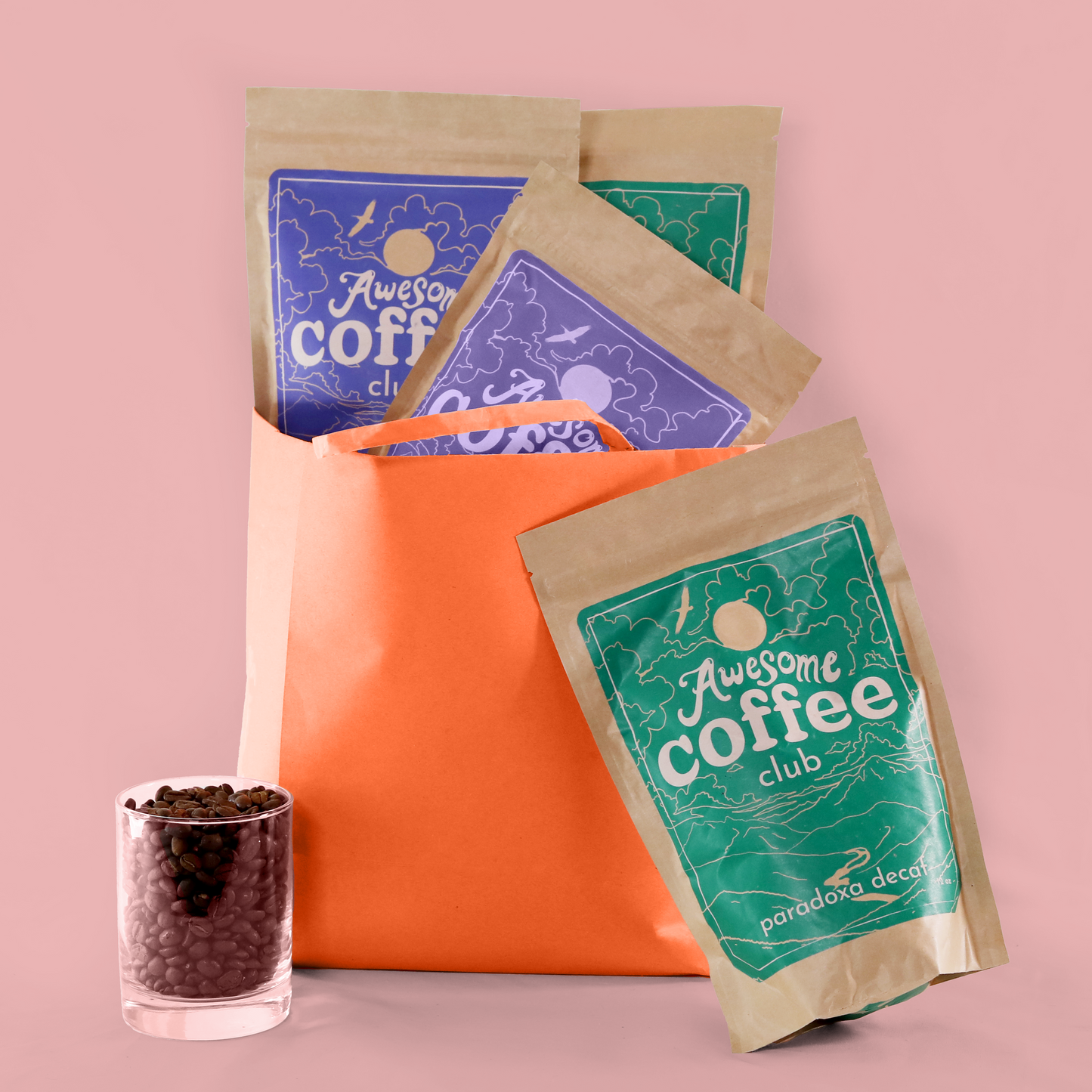 An orange paper bag filled with bags of Awesome Coffee Club Coffee with a bag of Paradoxa in front and a cup of coffee beans. A Good Store product.