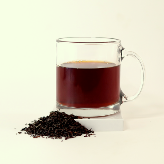A clear glass mug filled with dark reddish-brown tea - Bright Star Breakfast Blend -  next to a small pile of dried tea leaves. A Good Store product.