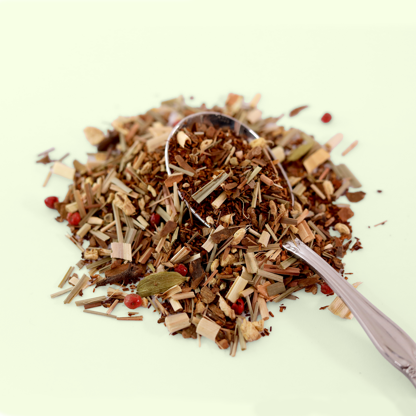 A close-up view of a pile of dried Evensong Chai tea leaves. A metal spoon is visible, scooping up some of the tea blend. A Good Store product.