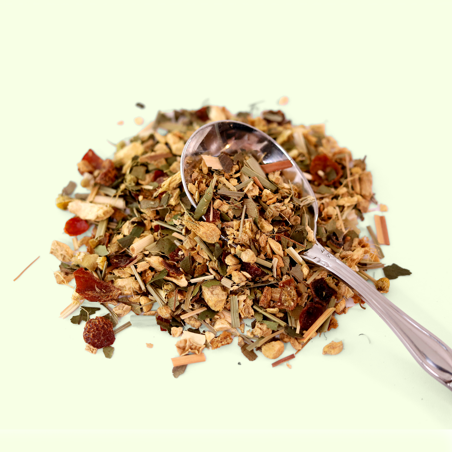 A close-up view of a pile of dried Golden Fire Ginger tea leaves. A metal spoon is visible, scooping up some of the tea blend. A Good Store product.