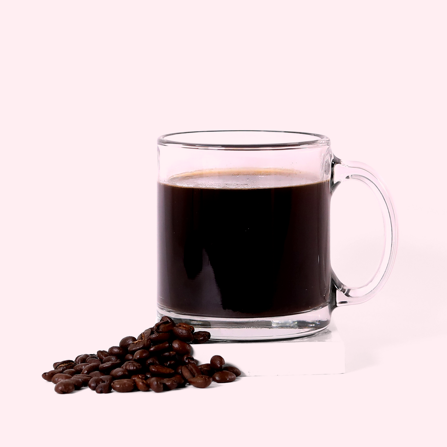 A clear glass mug filled with dark Octavia coffee. In front of the mug is a small pile of roasted coffee beans. The mug and beans are placed on a white surface against a light pink background. A Good Store product.