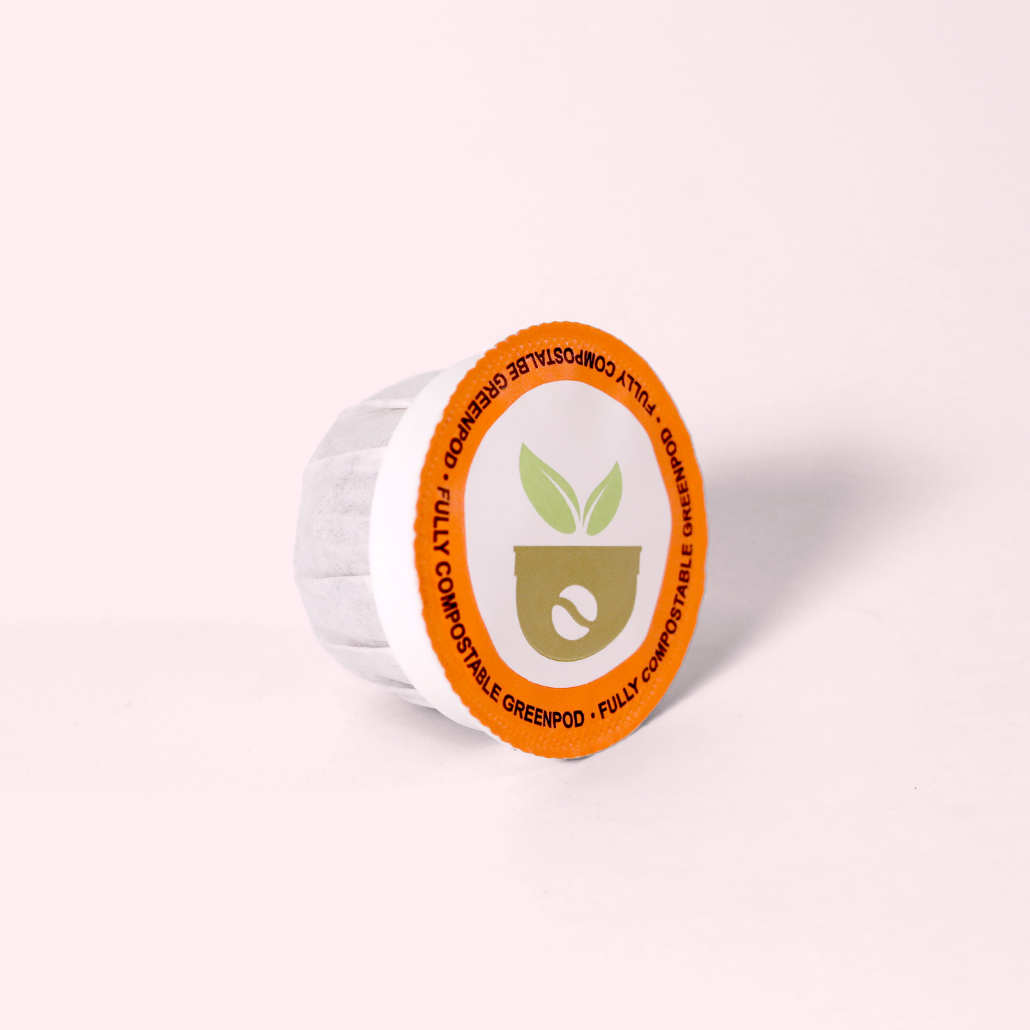 A single-serve coffee pod viewed from the top, displaying an orange circular label with a green leaf logo and text "FULLY COMPOSTABLE GREENPOD" around the edge.