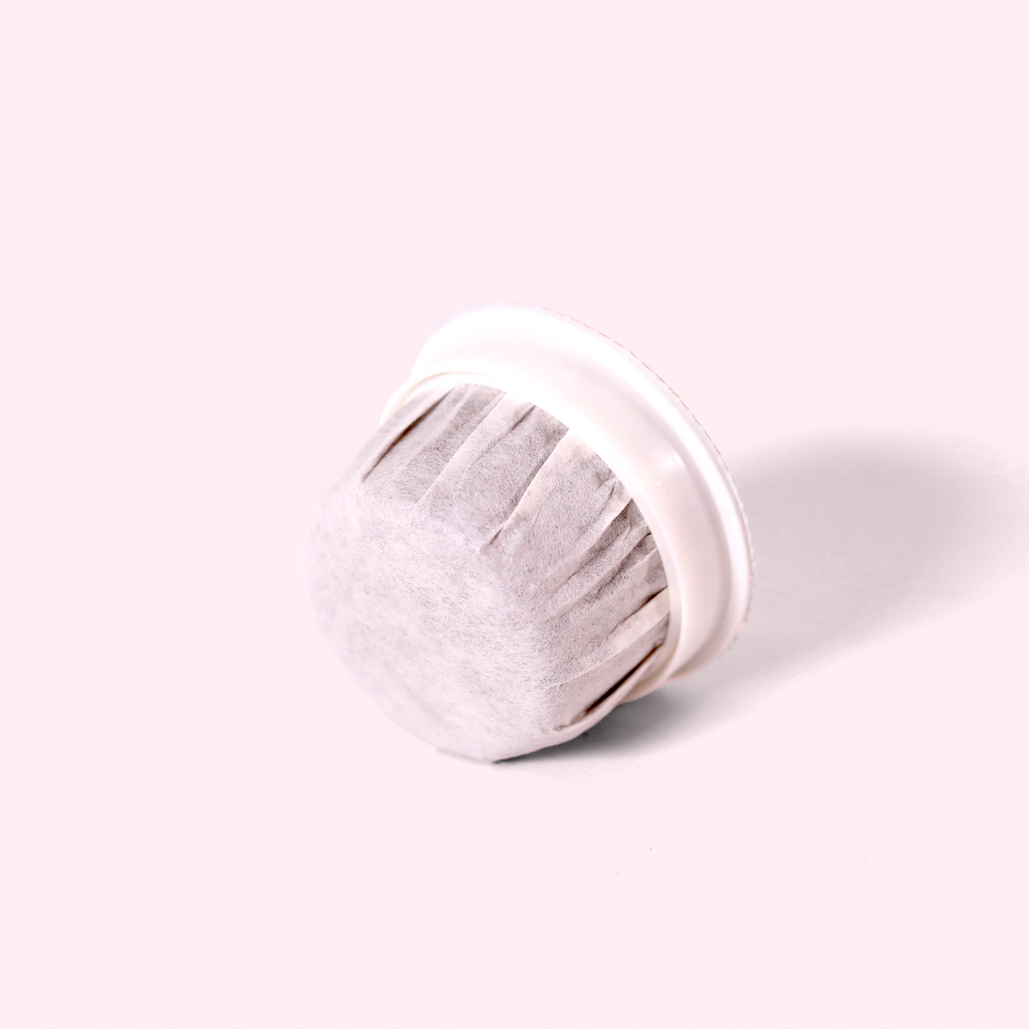 A close-up view of a single-serve coffee pod, showing the white filter bottom and plastic rim.