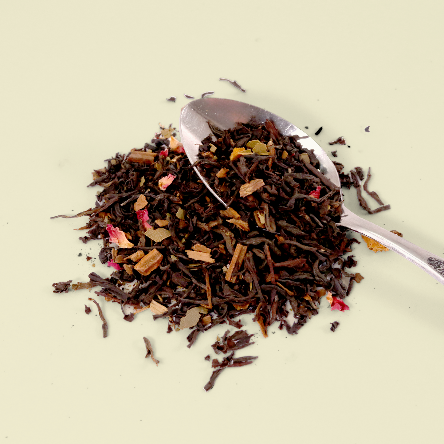 A pile of loose leaf tea on a light background. The tea appears to be a black tea blend with visible pieces of dried fruit or flower petals mixed in. A small silver spoon is partially visible in the tea pile. Keats & Co.