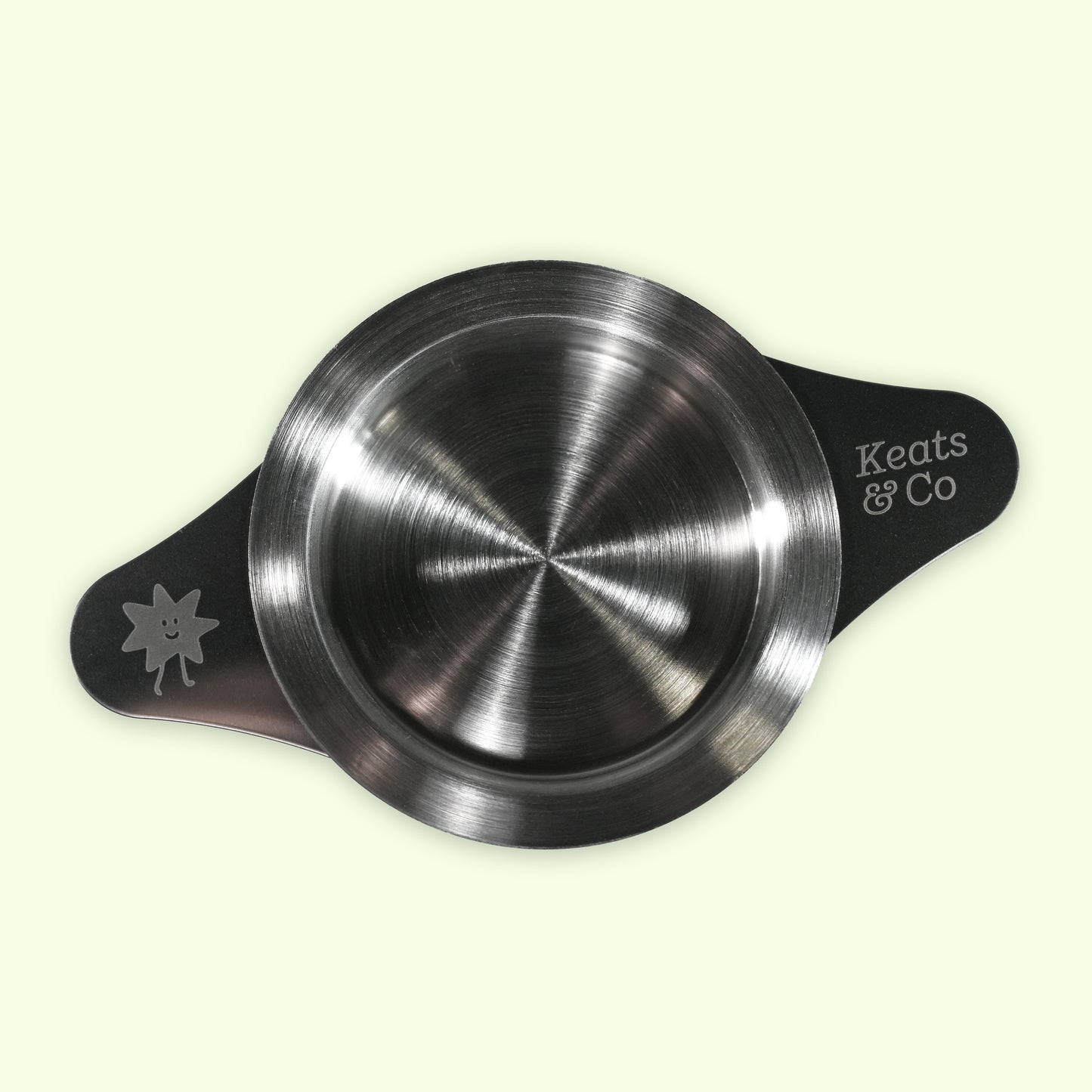 Metallic tea strainer with 'Keats & Co' branding on a light green background