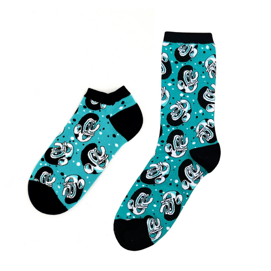 Two past designs from the Awesome Socks Club, one ankle, one crew, with a teal background, black heals and borders and black and white faces. A Good Store product.