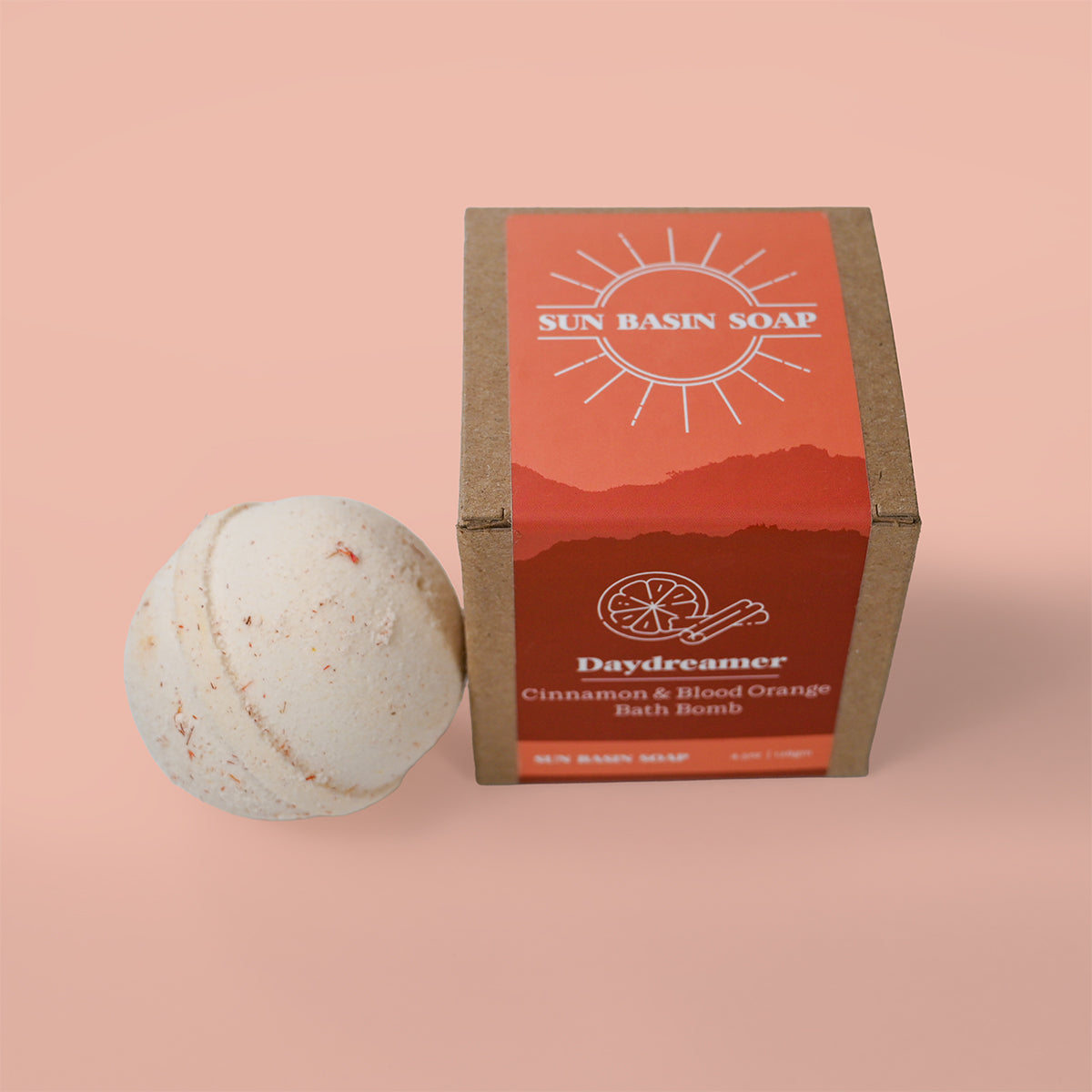 Bath bomb and packaging of Sun Basin Soap on a peach background