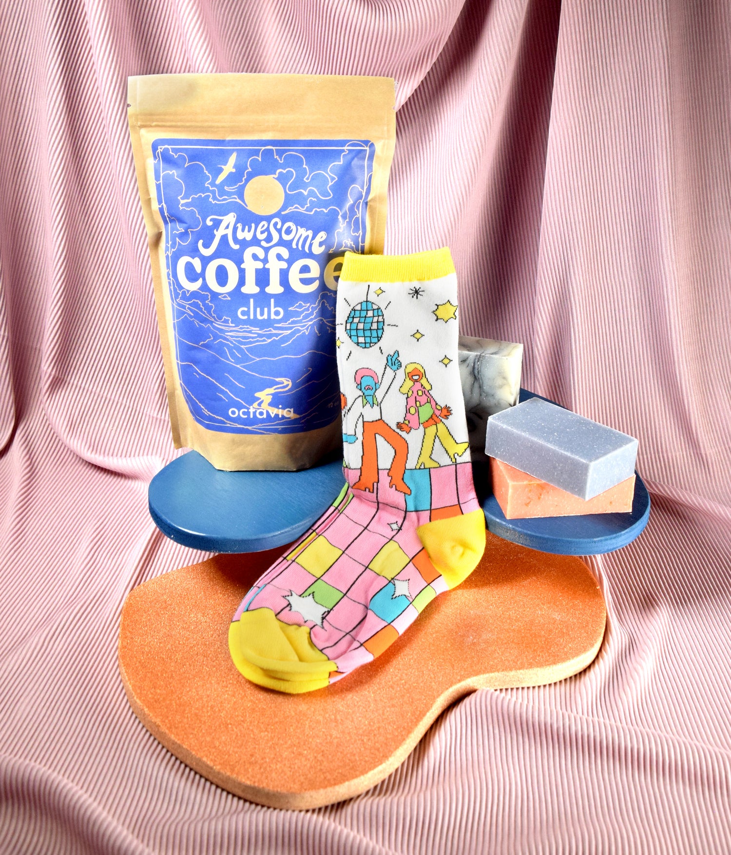 A bag of Awesome Coffee Club Octavia beans next to a colorful pair of Awesome Socks next to bars of soap from Sun Basin Soap.