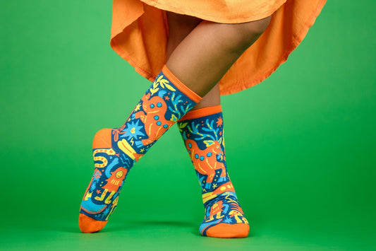 Image of a person from the knees down wearing a bright orange skirt and fun, colorful socks from Awesome Socks Club on a green background