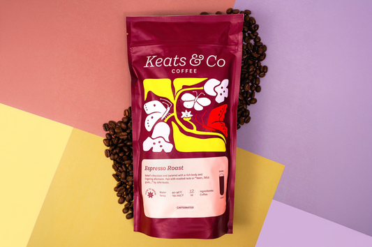 A bag of maroon Keats & Co Espresso roast over a colorful background surrounded by coffee beans