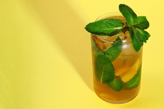 Glass of iced tea with mint leaves on a yellow background