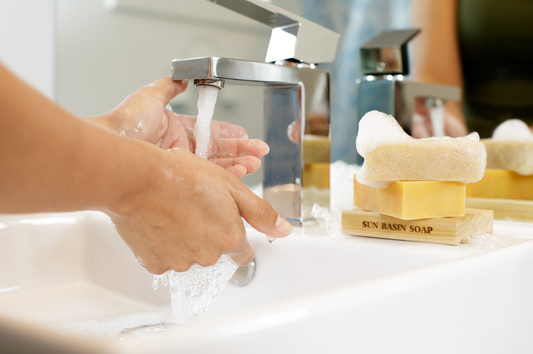 Image of hand washing in a sink. On the counter is a Sun Basin Soap soap holder with a stack of sudsy bar soap on top of it.
