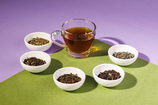 Image of a cup of tea in a glass mug surrounded by 5 small white bowls full of loose leaf tea from Keats & Co