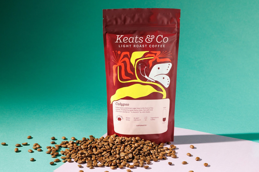Image shows a maroon bag of Keats & Co coffee on a table surrounded by roasted coffee beans