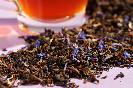 Image is a closeup of colorful loose leaf tea with a mug of tea in the background