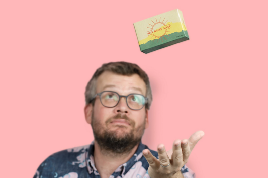 Image of John Green tossing a bar of Sun Basin Soap into the air over a pink background