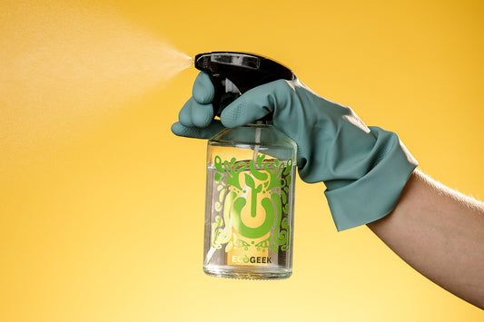 Hand in a green rubber glove holding a glass EcoGeek spray bottle and spraying the cleaning product 