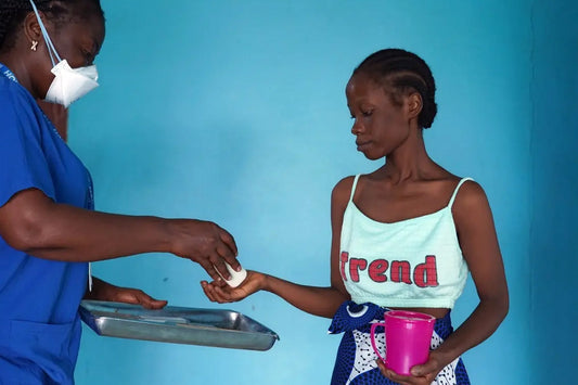 Image of a doctor in blue scrubs and a mask handing a cup of pills to a patient. 