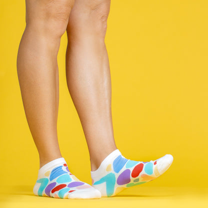 A yellow background showing two legs from the knee down, wearing ankle socks from the Awesome Socks Club with colorful blobs on them. A Good Store subscription product.