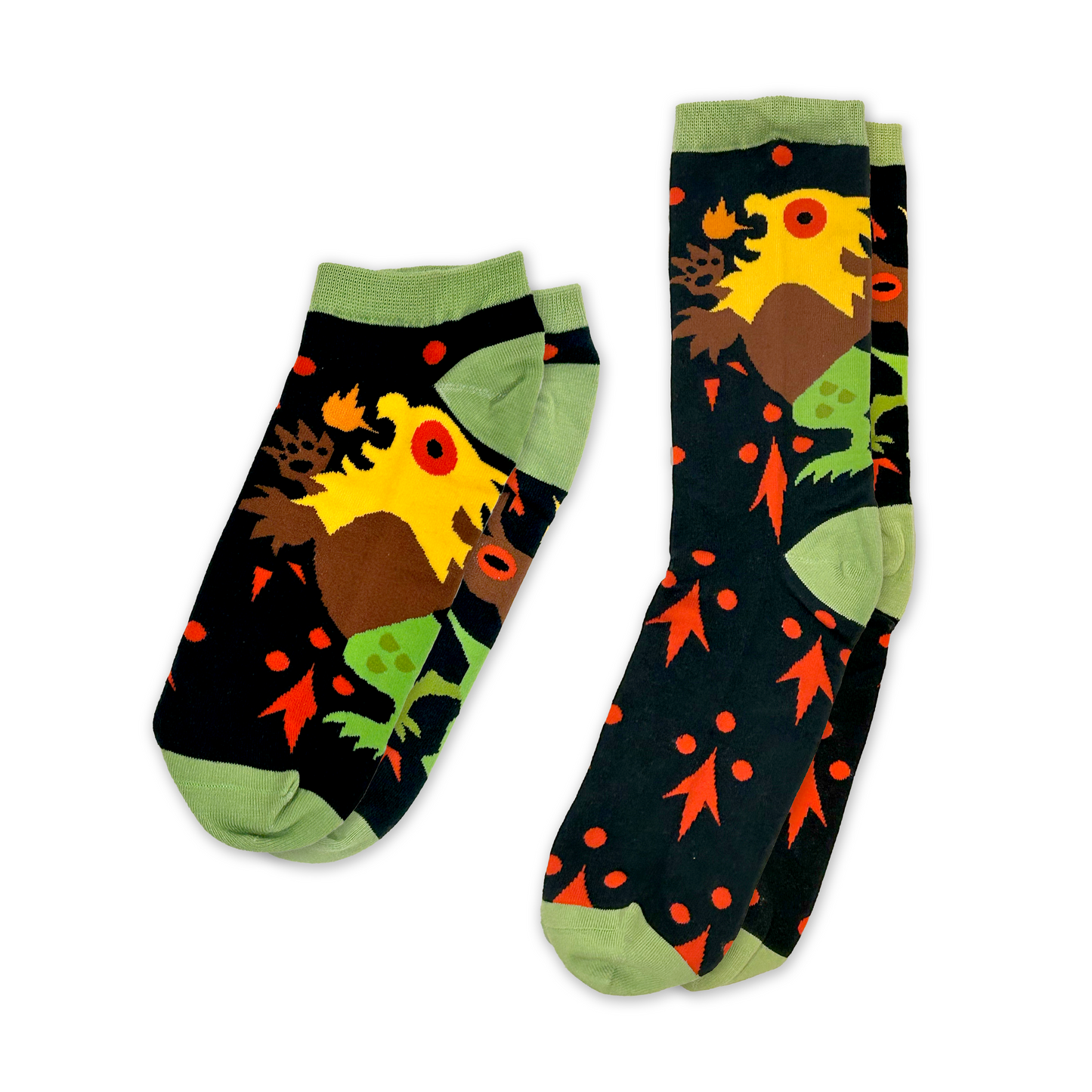 This image shows a pair of colorful, patterned socks. The socks feature a bold design with a large yellow Chimera as the main focal point. The background is primarily black, with orange leaf-like shapes and dots scattered throughout. The bird has a brown body, yellow head and crest, and green feet. The socks have light green cuffs, heels, and toes. Awesome Socks Club - Courtly Appeal. 