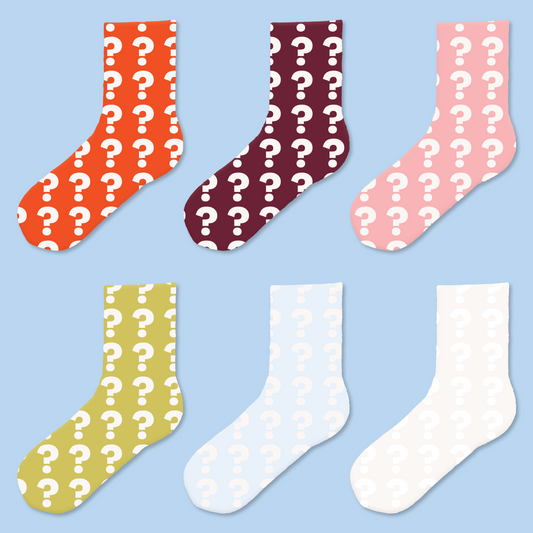 Six colorful socks arranged in two rows against a light blue background. The top row shows orange, burgundy, and pink socks, while the bottom row displays olive green, pale blue, and white socks. All socks feature a repeating white question mark pattern. 
