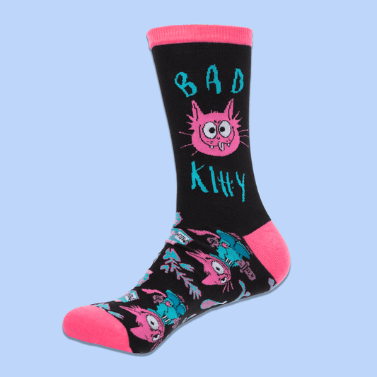A pair of black crew socks with bright pink toes, heels, and cuffs, featuring a colorful cartoon cat and teal text and pattern details, displayed against a light blue background.