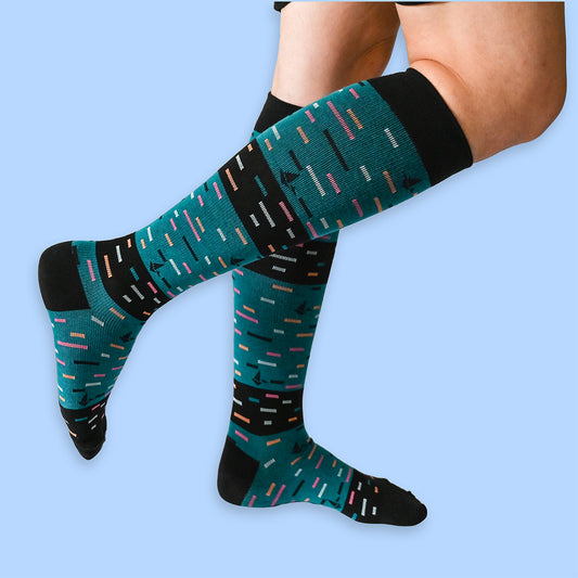 Teal and black patterned compression socks worn by a person on a light blue background