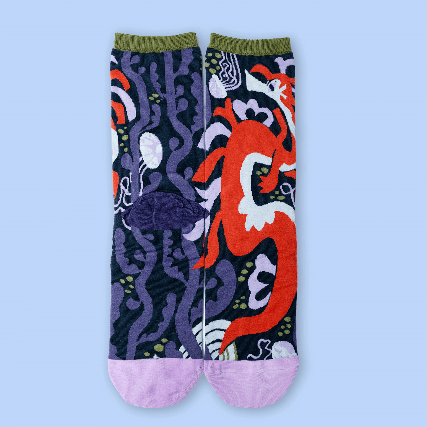 A pair of crew socks with a split design: one half features a dark navy and purple abstract pattern, and the other half features a large red dragon motif. The socks have olive green cuffs and light pink toes, shown against a solid light blue background.
