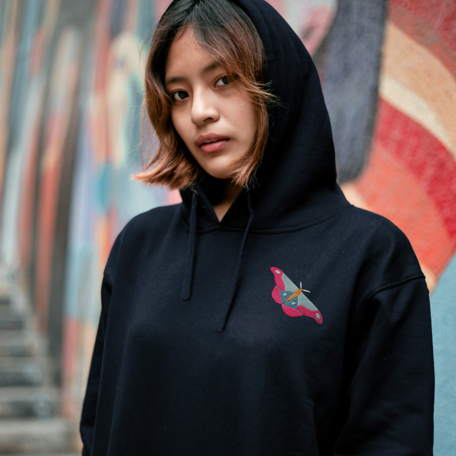 Person wearing a navy hoodie with a colorful logo against a graffiti-covered wall.