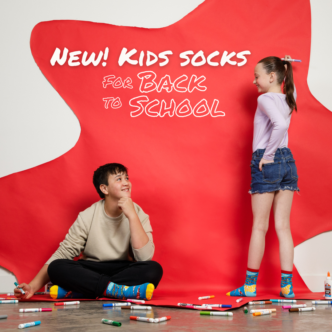 Two kids surrounded by markers in front of a large red star, looking at each other and smiling while wearing Awesome Socks. Text on the photo reads "New! Kids socks for back to school". A Good Store product. 