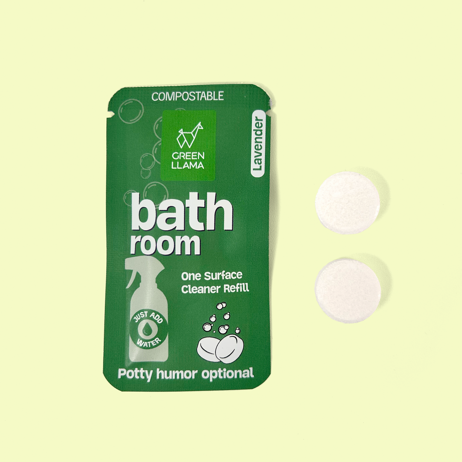 A green package of Green Llama bathroom cleaner refill tablets in lavender scent. The compostable packaging shows "bathroom" in large white text, with "One Surface Cleaner Refill" underneath. It displays "JUST ADD WATER" on a spray bottle icon. Two white circular cleaning tablets are positioned to the right of the package. At the bottom of the package, it humorously notes "Potty humor optional." Bathroom cleaning tabs from EcoGeek a Good Store product.