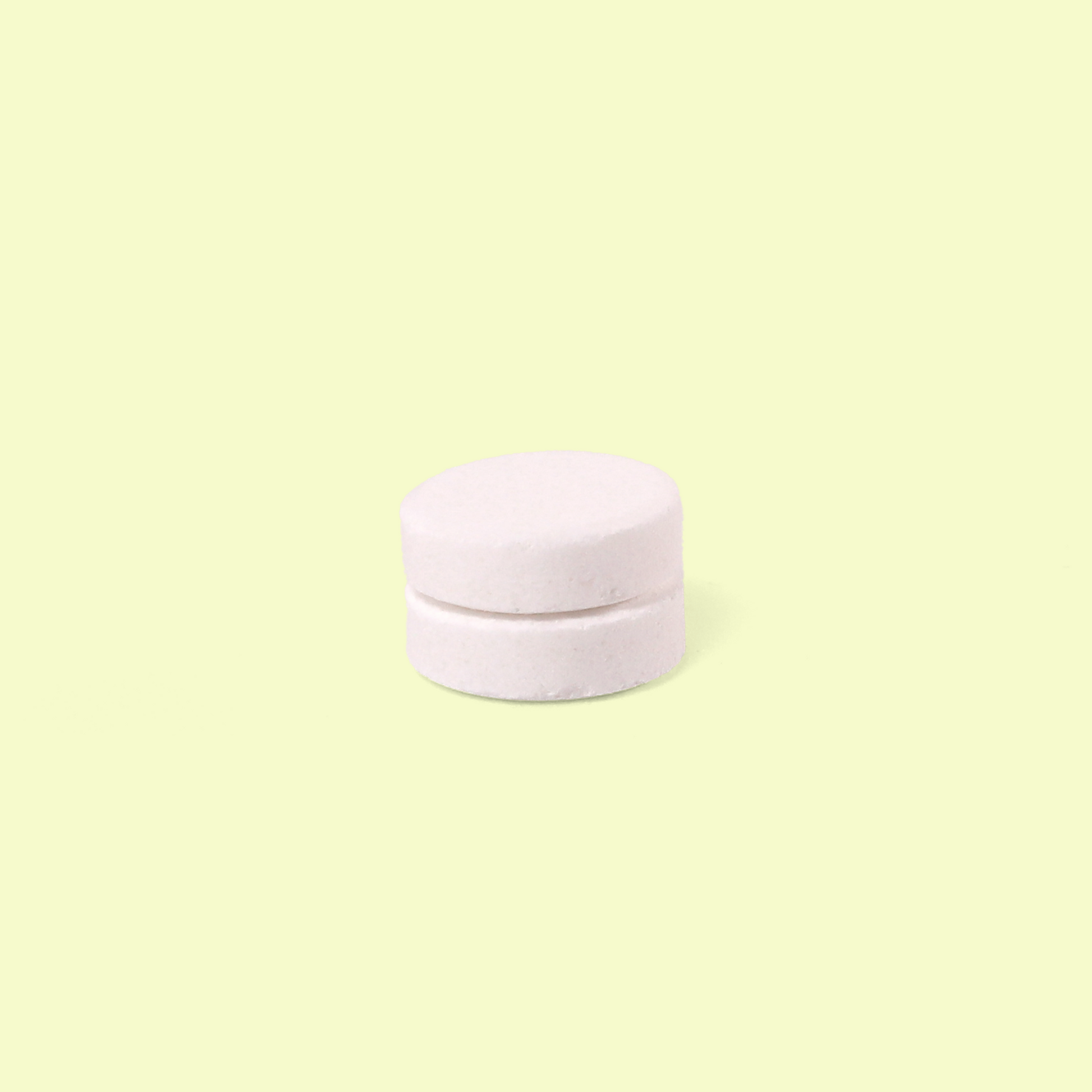 Two white circular cleaning tablets stacked on top of each other against a pale yellow background. Bathroom cleaning tabs from EcoGeek a Good Store product.