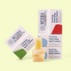 Product display of Meliora Cleaning Products foaming hand soap refill tablets showing three varieties: a green-bottom box of lemongrass scented tablets on the left, a stack of yellow soap bars in the center, and two blue-bottom boxes of unscented tablets stacked on the right, all with red and white packaging featuring the Meliora logo, photographed against a pale yellow background