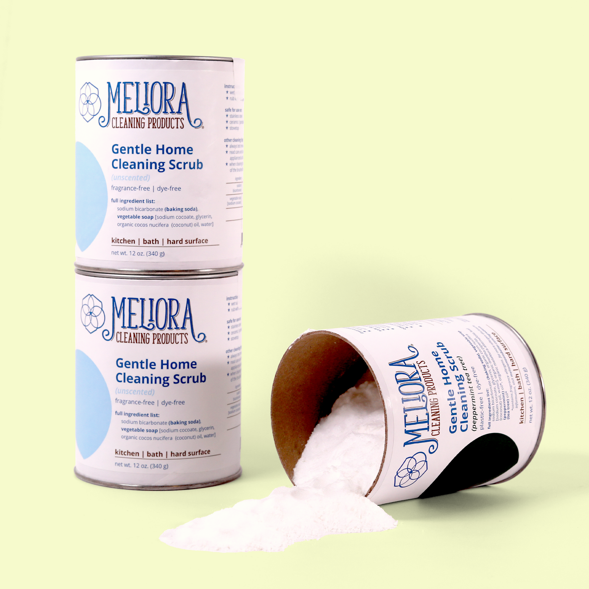 Three containers of Meliora Gentle Home Cleaning Scrub against a pale yellow background. Two upright containers are labeled as unscented, while a third container is tipped on its side with white powder spilling out. Each metal container features the Meliora logo and lists ingredients including baking soda and vegetable soap, designed for use on kitchen, bath, and hard surfaces. Gentle home cleaning scrub from EcoGeek a Good Store product.