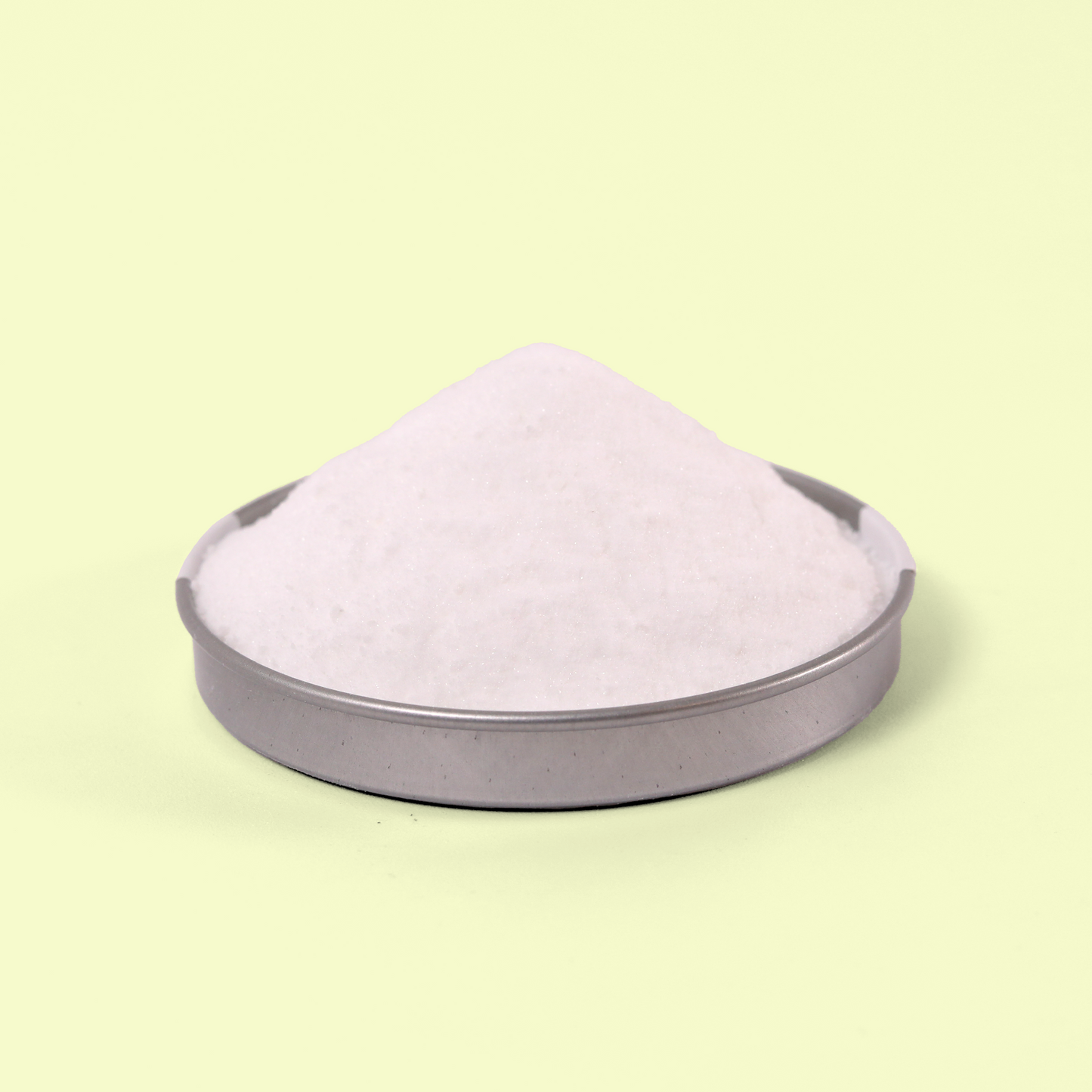 A close-up of a metal lid holds the conical pile of powder displayed against a pale yellow background, showcasing the powdery texture of the cleaning product. Gentle home cleaning scrub from EcoGeek a Good Store product.