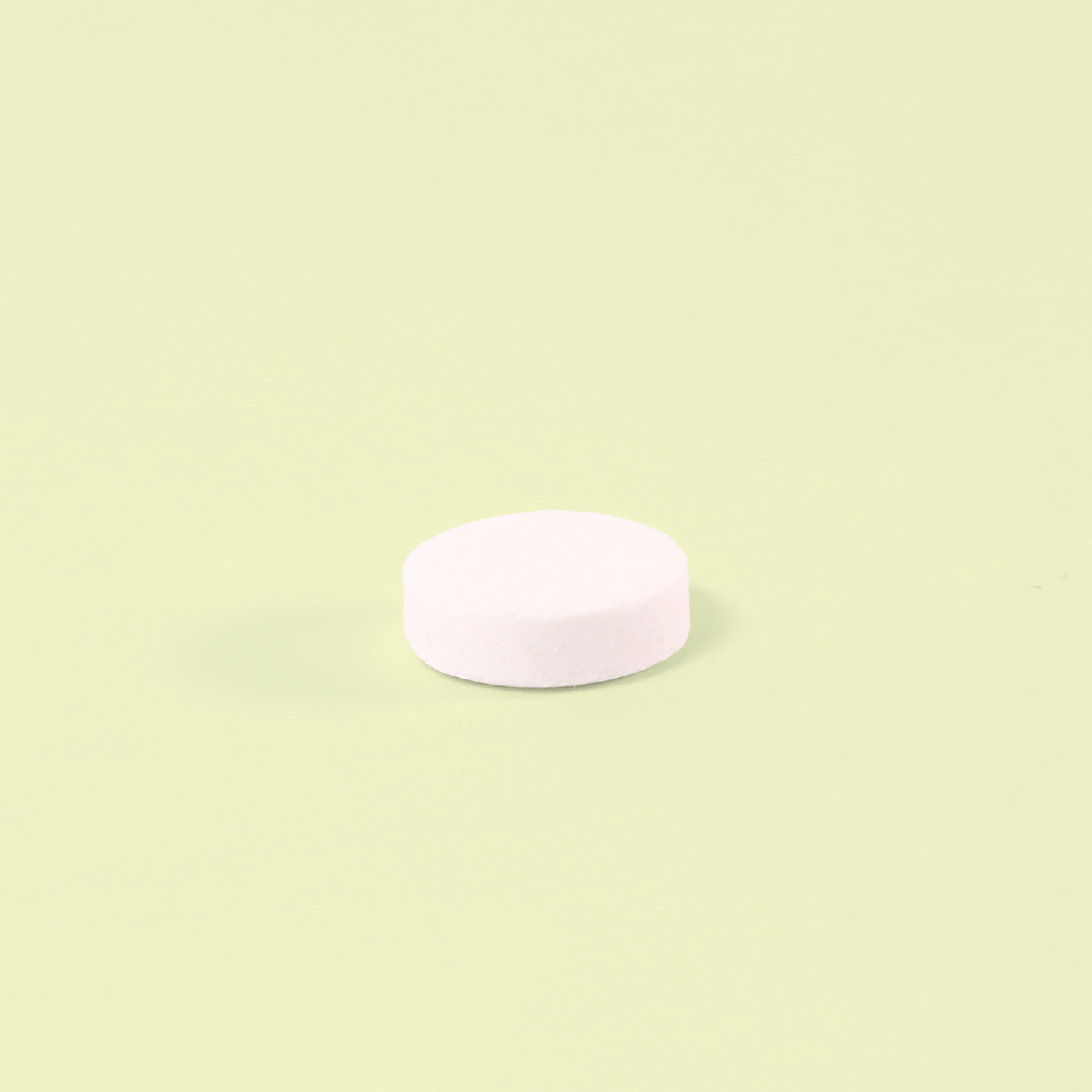 Two white circular cleaning tablets stacked on top of each other against a pale yellow background. Glass cleaning tabs from EcoGeek a Good Store product.