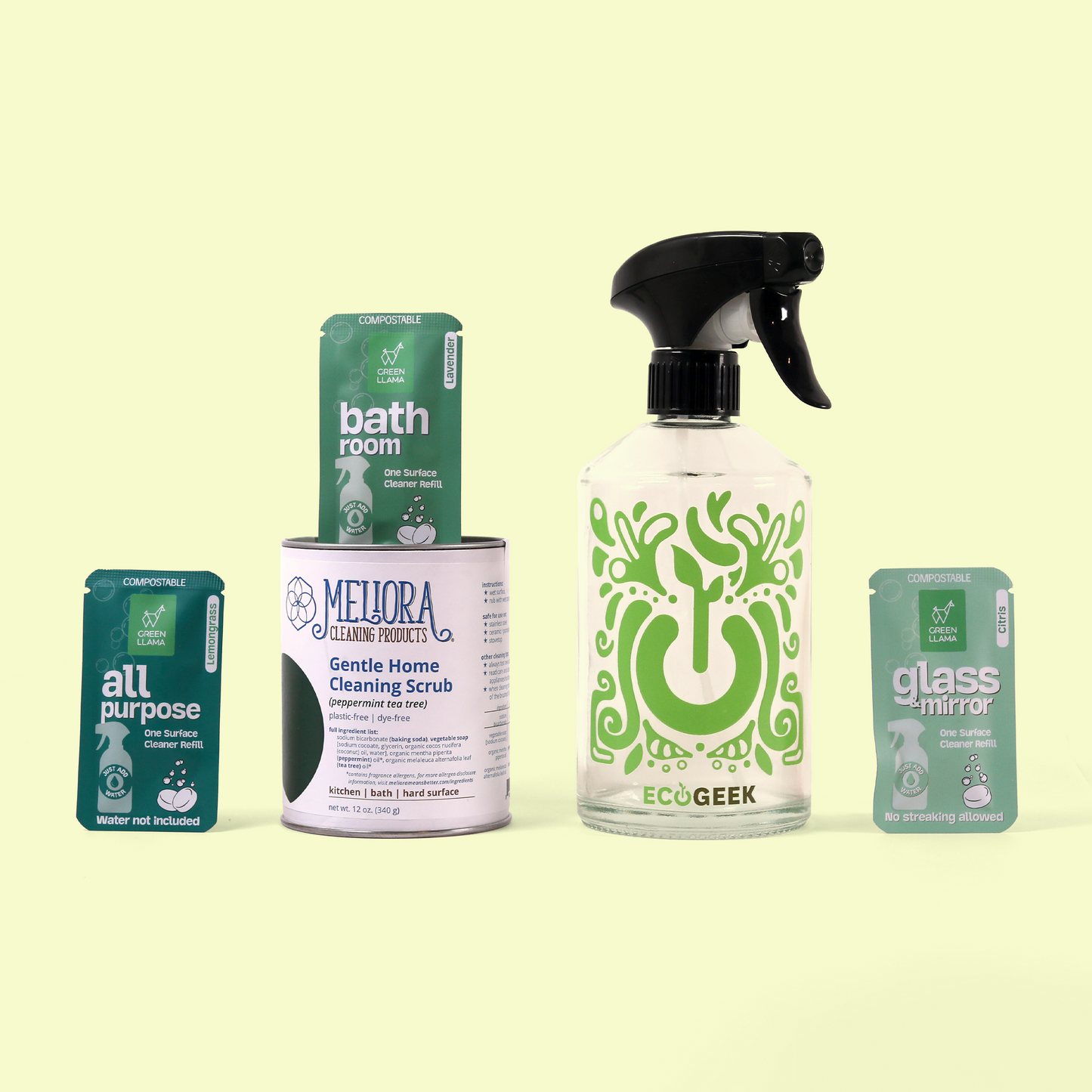 A collection of eco-friendly cleaning products displayed against a pale yellow background. Featured items include three Green Llama compostable cleaner refill packets (all purpose, bathroom, and glass & mirror), a Meliora Gentle Home Cleaning Scrub container in peppermint tea tree scent, and an ECOGEEK glass spray bottle with black trigger sprayer featuring a decorative green power button design. Home cleaning bundle from EcoGeek a Good Store product.