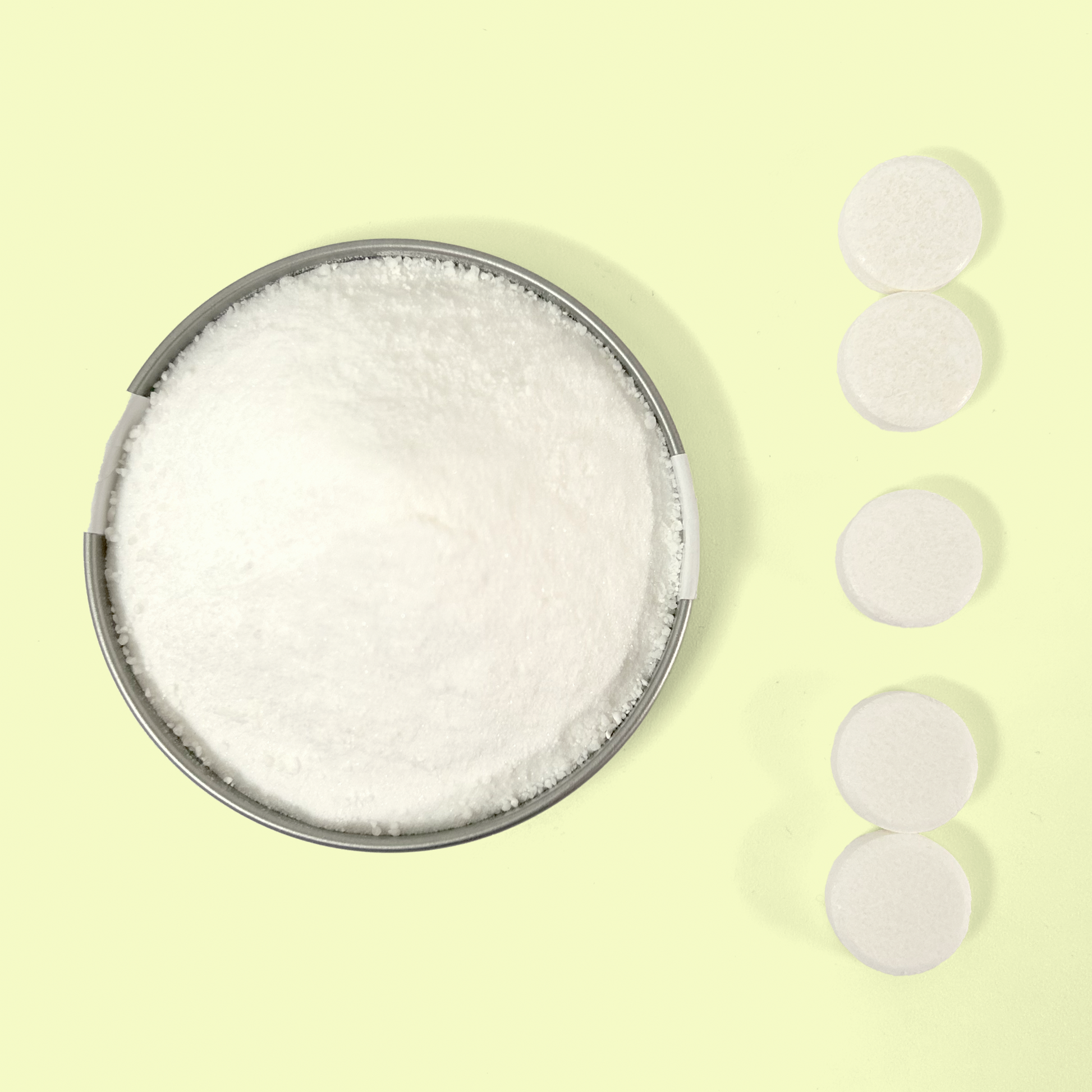 A circular metal container filled with white powder cleaning product, likely a powdered cleaner, displayed beside a vertical row of five white circular cleaning tablets against a pale yellow background. The image shows the contrast between the loose powder form and the compressed tablet form of eco-friendly cleaning products. Home cleaning bundle from EcoGeek a Good Store product.