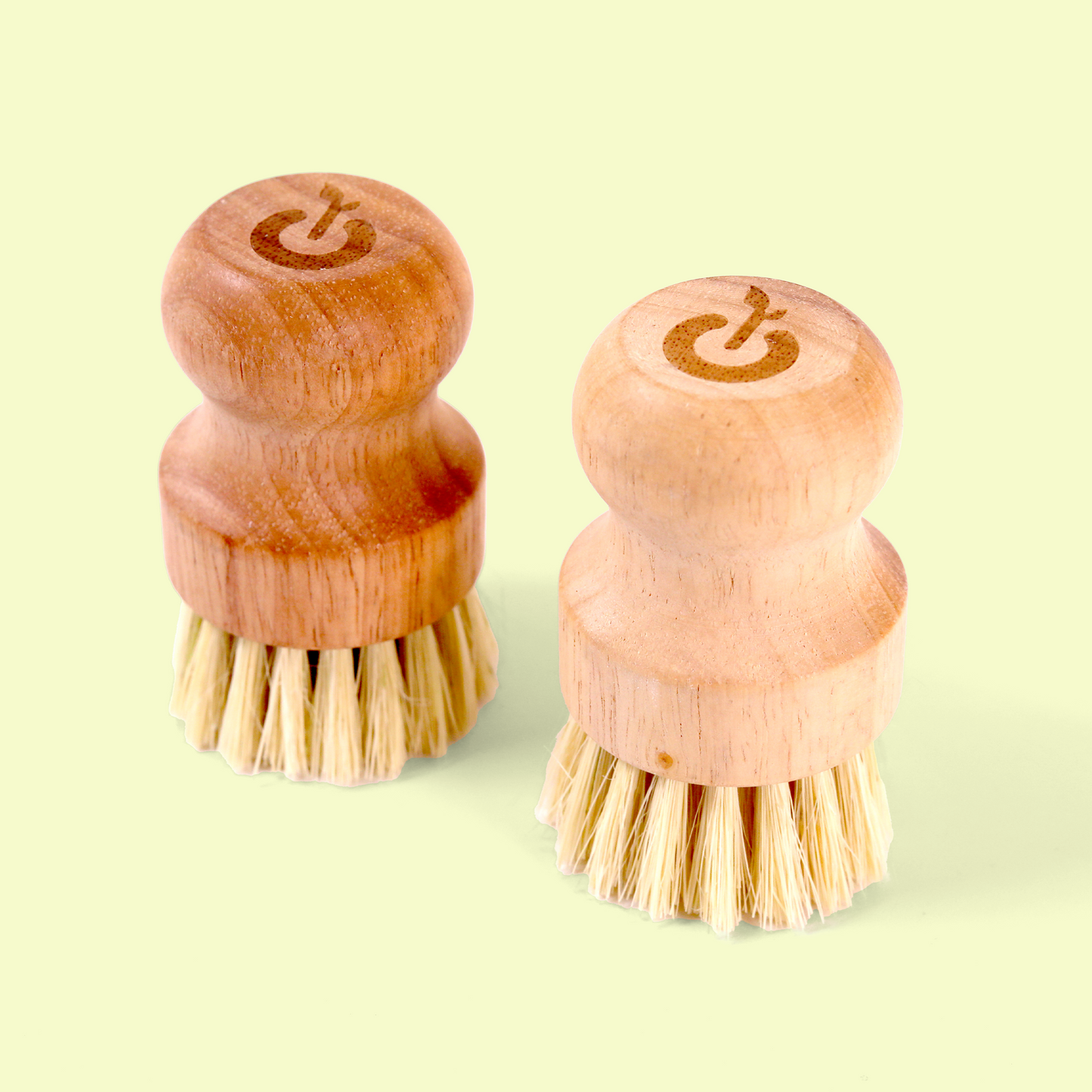 Two compact wooden scrub brushes positioned with bristles facing down. Both have power button/on-off symbols engraved on their tops. The brushes appear to be designed for kitchen or dish cleaning with their short natural bristles and ergonomic wooden handles. Wood dish scrub brush from EcoGeek a Good Store product.