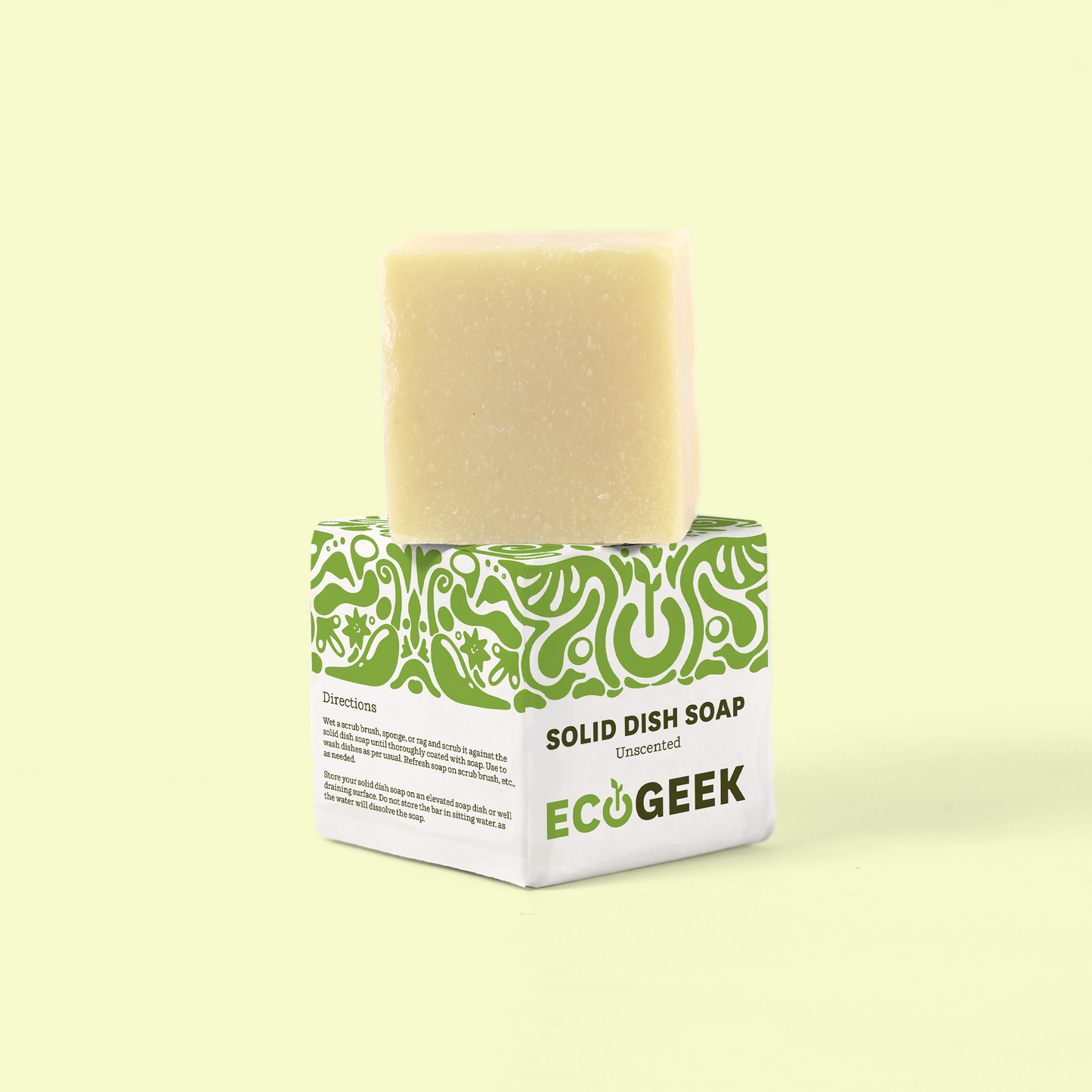 The image shows a bar of unscented solid dish soap from the brand "ECOGEEK." The soap is a light beige/cream color and sits atop its green and white packaging. The packaging features a decorative green swirly pattern on the top portion and "SOLID DISH SOAP [Unscented]" written prominently. The ECOGEEK logo appears at the bottom of the packaging. The entire product is photographed against a pale yellow background, creating a clean, minimalist presentation. Solid dish soap from EcoGeek a Good Store product.