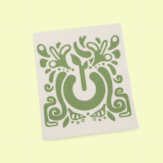 A single white square dish cloth featuring a decorative green design on a pale yellow background. The design shows an ornate, folk art-style tree with flourishing branches, leaves, and botanical elements arranged in a symmetrical pattern around a central curved trunk.