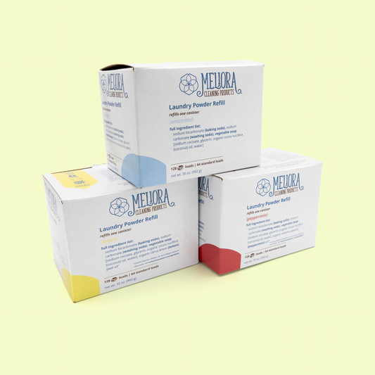 Three Meliora Cleaning Products Laundry Powder Refill boxes stacked and arranged together, showing three different scent varieties: lemon (yellow accents), unscented (blue accents), and peppermint (red accents). All boxes feature the same white design with the geometric flower logo and product information