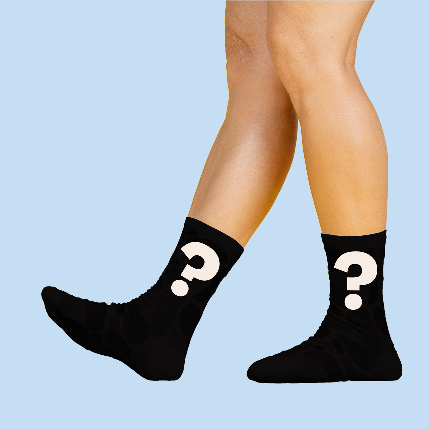 A pair of legs wearing black socks with white question mark symbols against a light blue background. The socks are shown in a standing position, with the question marks prominently displayed on the sides.