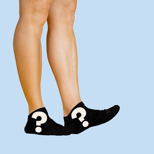 Legs and black socks with white question marks. The socks appear shorter in height than in the first image, resembling ankle socks rather than crew socks