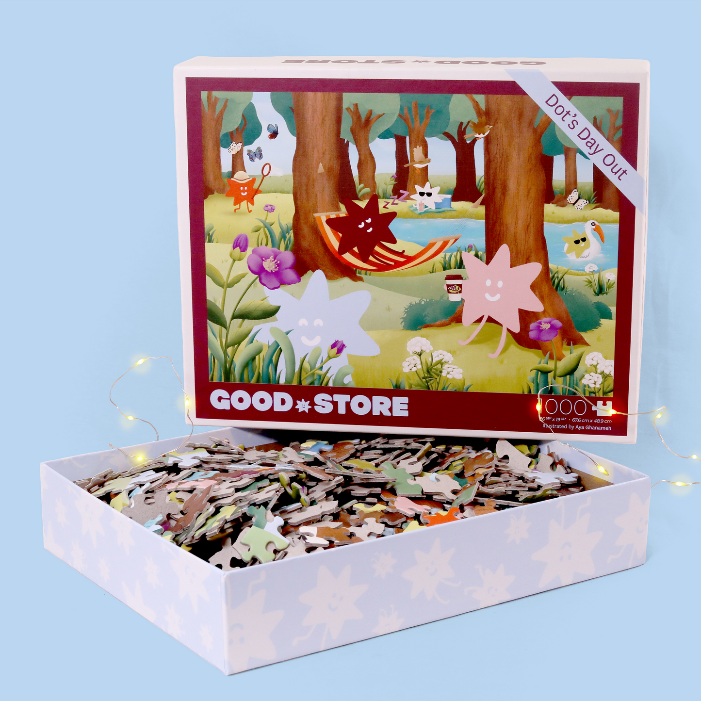 A 1000-piece puzzle box from "Good Store" showing a whimsical woodland scene with star-shaped characters relaxing in a forest. The illustration includes a red star in a hammock, purple flowers, and other stars enjoying a day out. The box is decorated with the brand's burgundy star logo and photographed against a light blue background with tiny fairy lights.