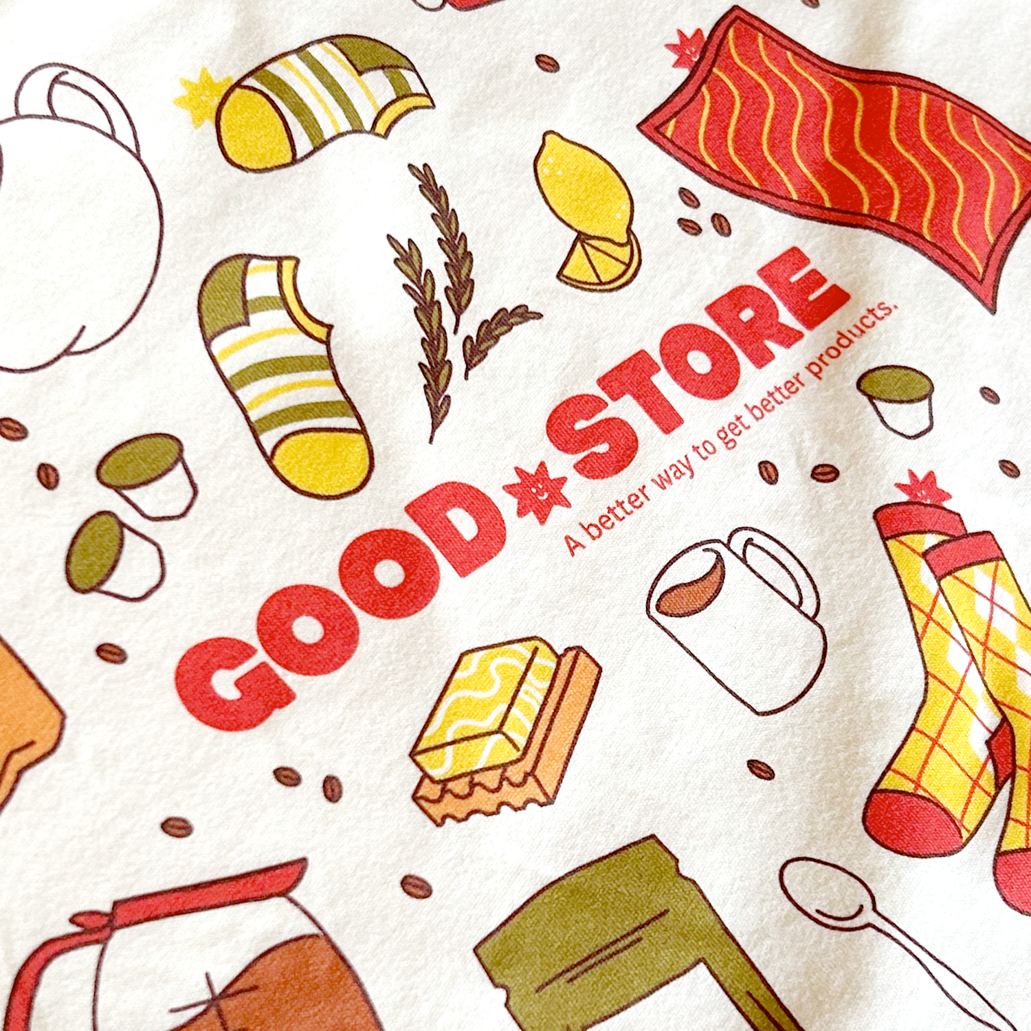 A full view of the beige t-shirt displaying the complete front design with all the colorful food illustrations arranged in a circular pattern around the central "GOOD STORE" branding and tagline