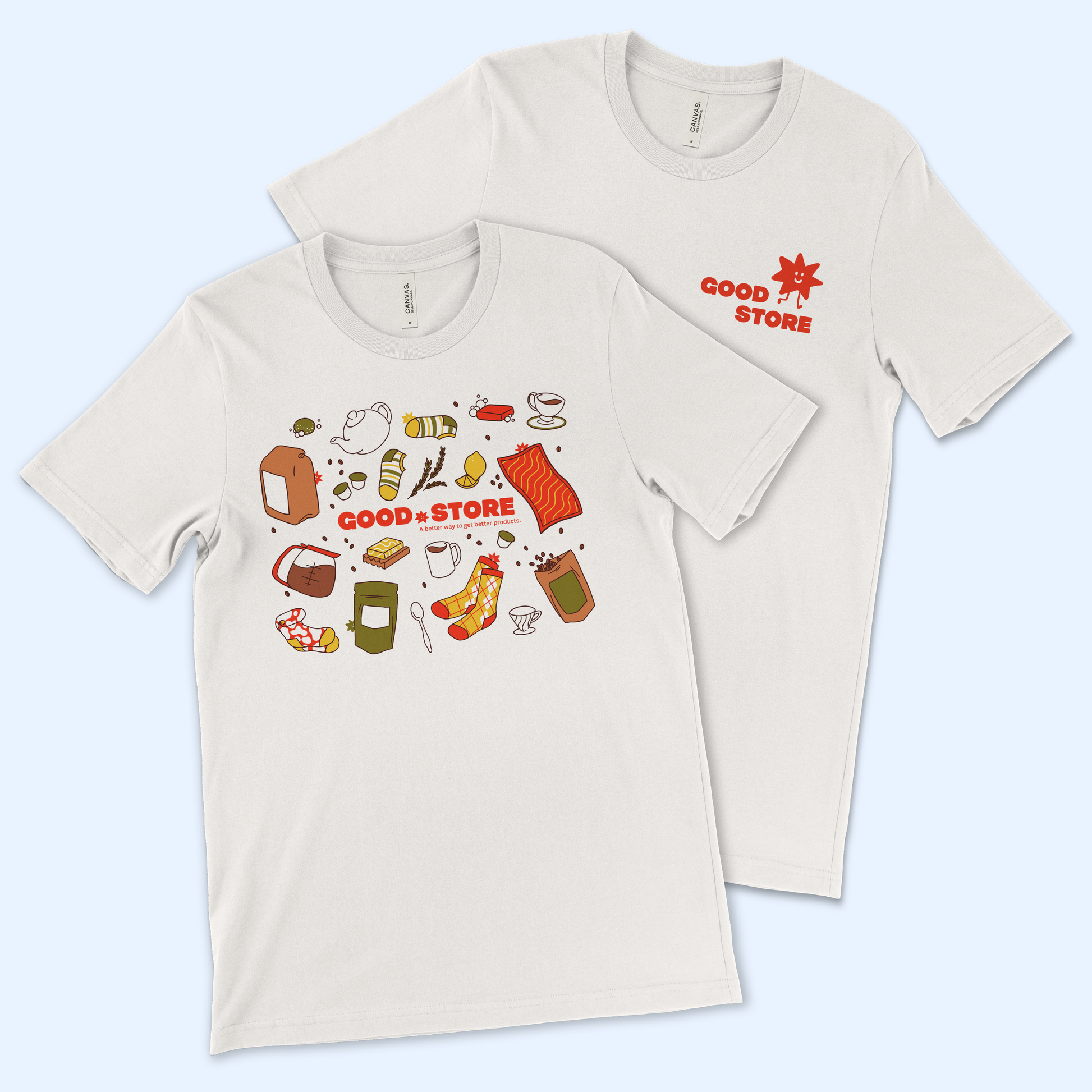 Two beige t-shirts on a light blue background. The front shirt displays colorful food illustrations including bread, teapots, salmon, coffee cups, and other grocery items surrounding red text reading "GOOD STORE" with the tagline "A better way to get better products." The back shirt shows a simple red "GOOD STORE" logo with a smiling star character.