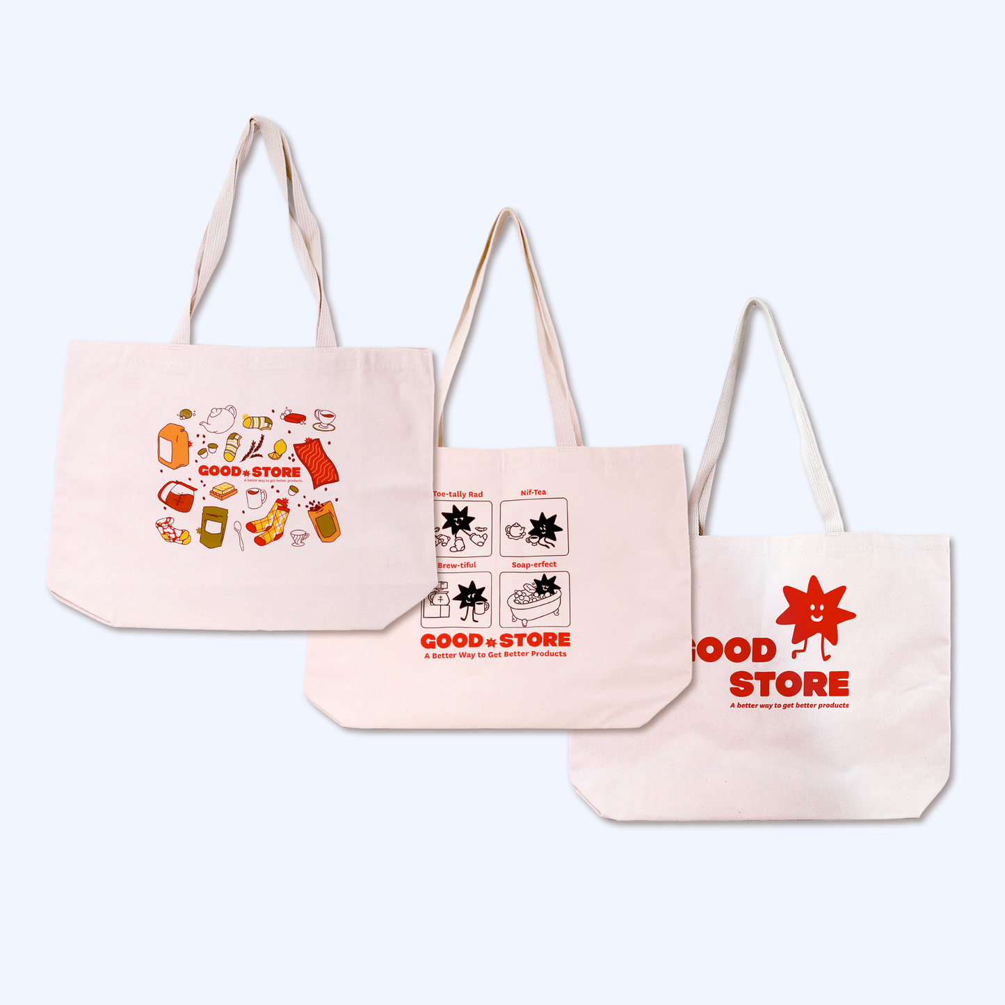 Three cream-colored canvas tote bags from Good Store displaying different designs. Left bag features colorful product illustrations including tea, socks, and bath products. Middle bag shows a comic-style grid with the store's star mascot in various tea-related activities labeled "Too-tally Red" and "Nil-Tea." Right bag has the minimal Good Store logo with their red star mascot and tagline "A better way to get better products." All bags are arranged in descending size order against a white background.